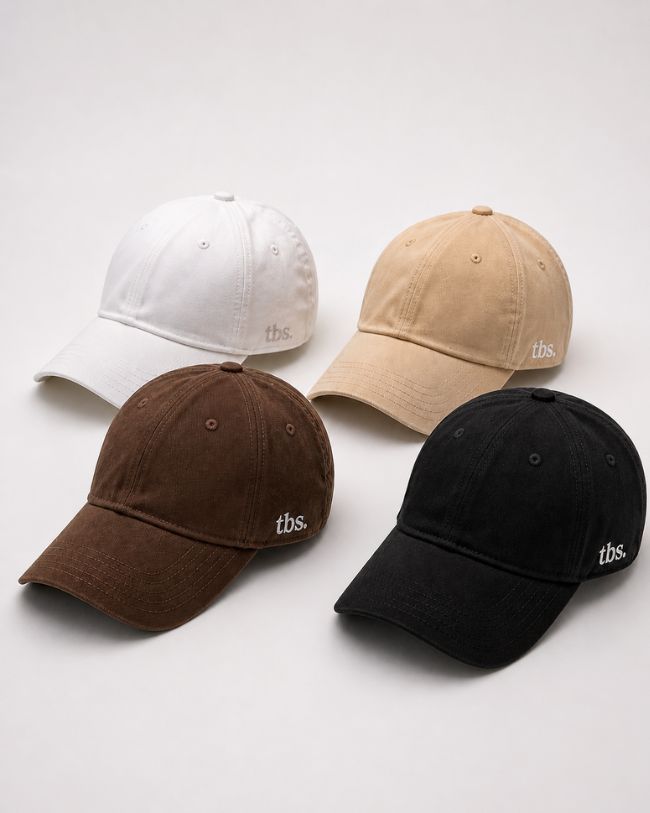 Four baseball caps in white, beige, brown, and black on a light gray background.